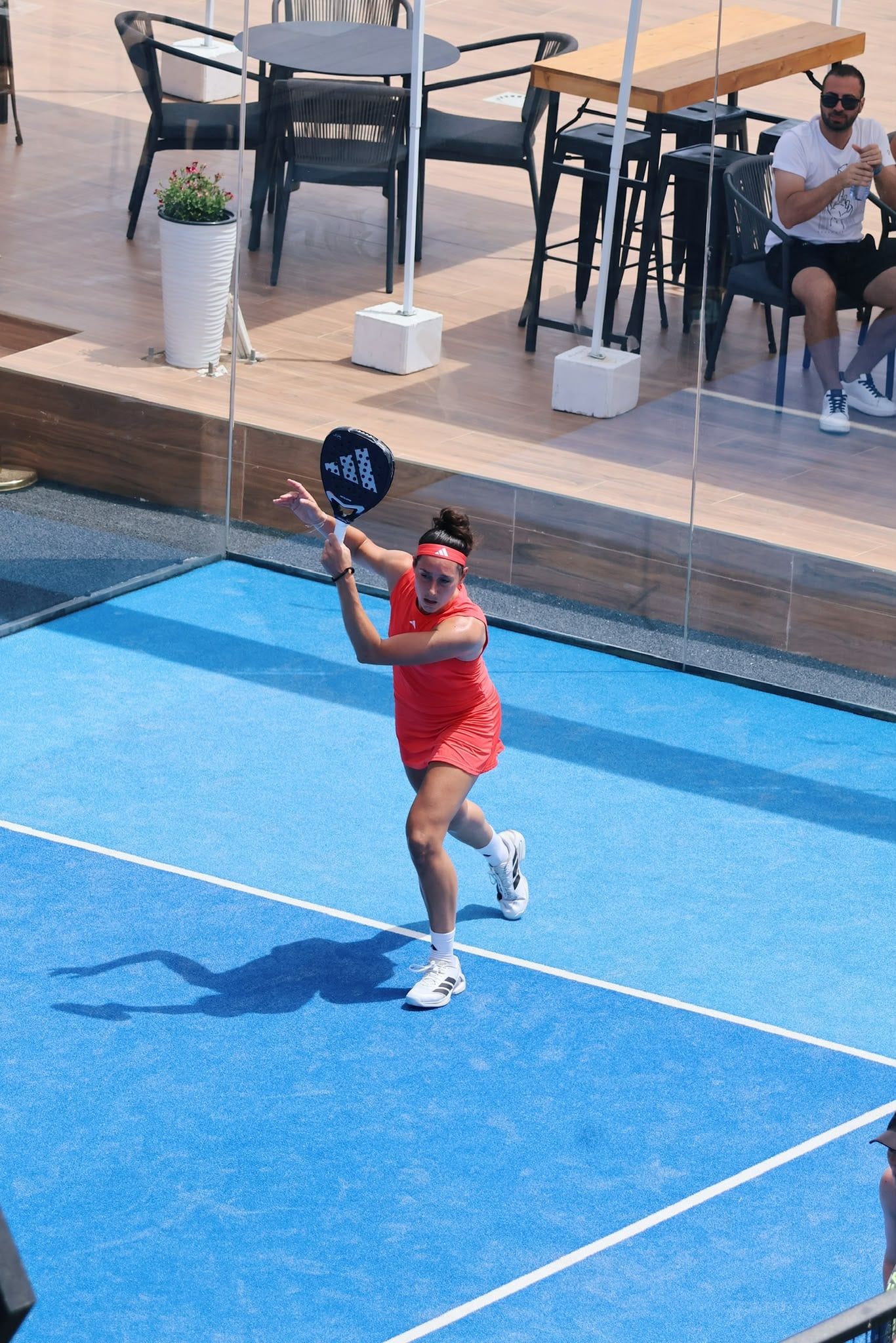 Padelspeelster in actie met terras en publiek op de achtergrond